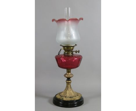 A large Victorian oil lamp with painted metal base, faceted ruby glass font and etched glass shade and chimney.
