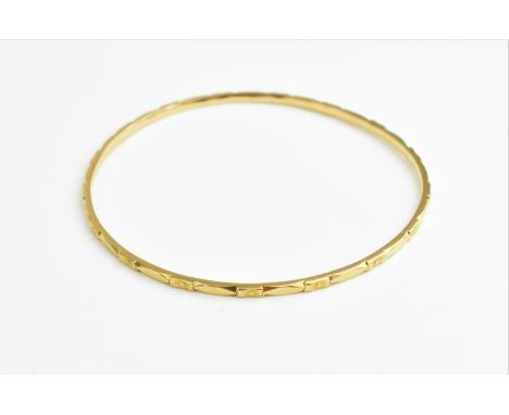 A yellow metal bangle with repetitive floral pattern detail, 6.5 cm diameter, tests as 18ct gold, 10 grams 