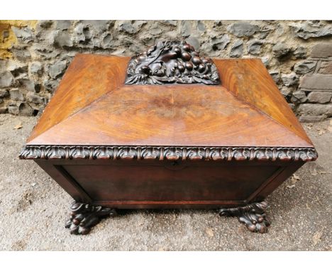 A Regency period flame mahogany sarcophagus form cellarette, with thick moulded acanthus border, the hinged lid with fruit fi