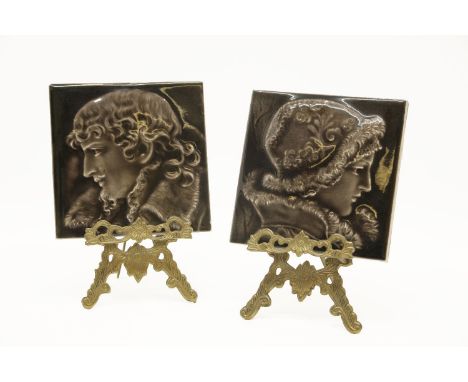 A pair of brass miniature easels, and a pair of portrait tiles