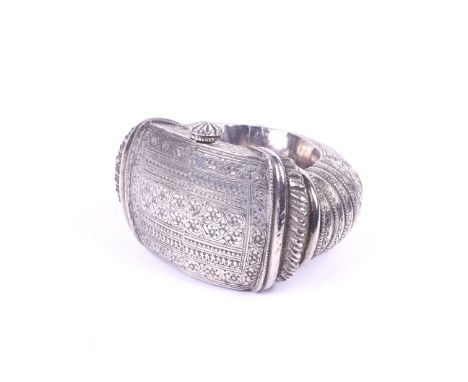 A white metal Indian slave bangle. Decorated with dense chased patterns of bands, leaves and scrolls, fixed with a pin. Weigh