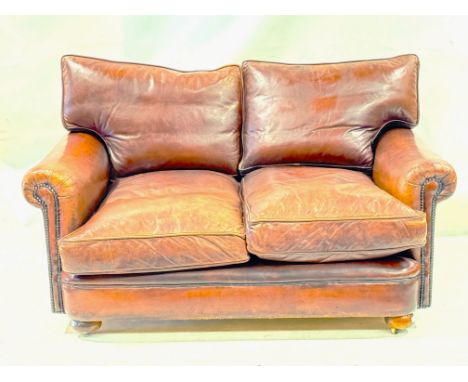 A two seater brown leather sofa. With scroll arms and stud detail raised on casters. L140cm x D100cm x H82cm