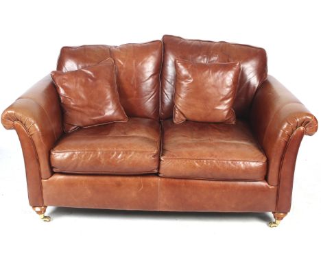A two seater brown leather sofa. Having scroll arms, on turned wooden supports with brass casters, together with two matching