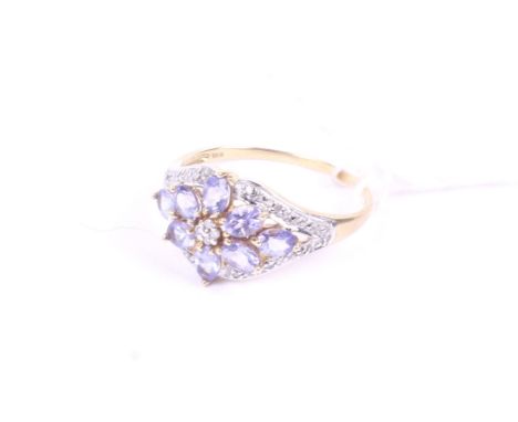 A modern 9ct white and yellow gold, tanzanite and diamond flower-head cluster ring. The central cluster within a scrolling-ri