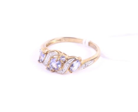A modern 9ct gold, tanzanite and diamond cross-over scroll ring. The three central graduated round pale-blue tanzanites betwe