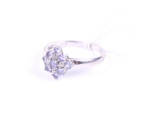 A modern 9ct white gold, tanzanite and diamond flower-head cluster ring. The nine small round tanzanites with four small diam