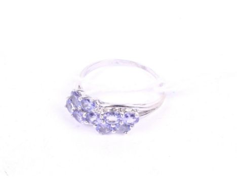 A 9ct white gold and tanzanite nine-stone cross-over ring. The oval mixed-cut pale blue tanzanites all claw set in a 'wavy' t