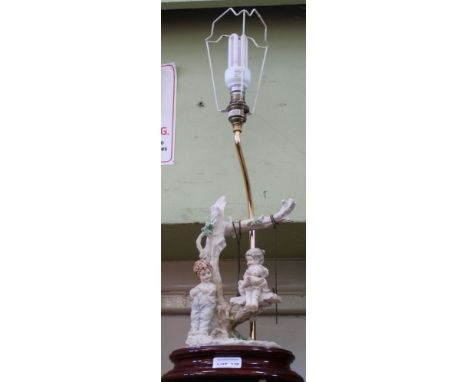 AN ITALIAN MADE FIGURAL TABLE LAMP depicting a young boy &amp; girl, she on a swing, complete with tasselled shade 