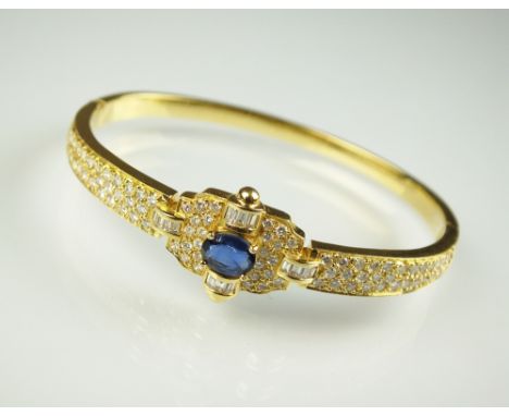 A sapphire and diamond hinged bangle, designed as a central oval mixed cut sapphire flanked by four arches of baguette cut di