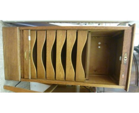 An early 20thC light oak pedestal office filing cabinet, having a rising tambour front, enclosing sliding shelves, on a plint