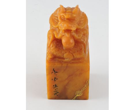 A Chinese amber soapstone seal carved with a seated dragon with pearl over etched gilt band, H 11 cms.