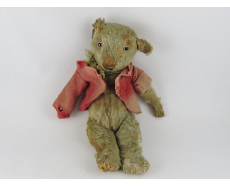 A mid-20th century teddy bear, golden plush with a stitched nose and button eyes, wearing a red jacket and green scarf L. 38c