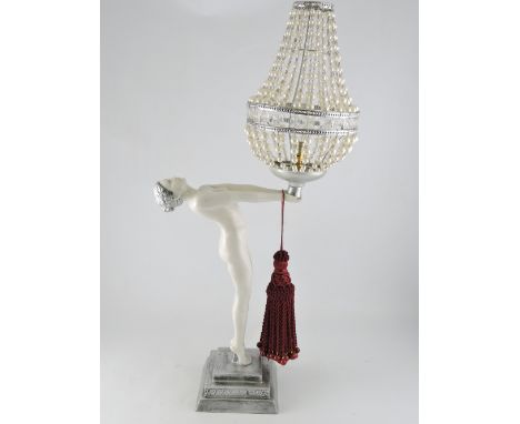 An Art Deco style table lamp in the form of a standing nude, arms outstretched holding a faux pearl shade, on a stepped squar