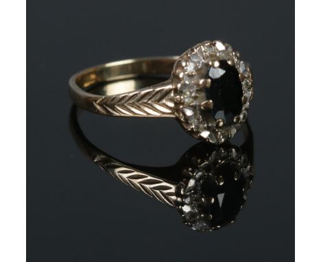 A 9ct Gold and black stone ring, with central stone surrounded by an illusion set border on part chevron decorated band. Size
