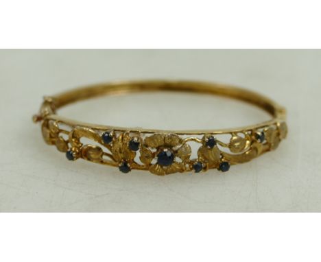 9ct hallmarked gold bangle with floral decoration, set sapphires. 14.1g.