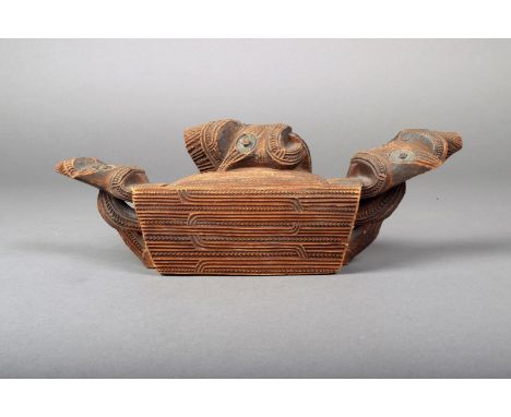 A Maori wood tinder box, rectangular with allover carved with linear and notched designs, the ends with tiki heads on open su