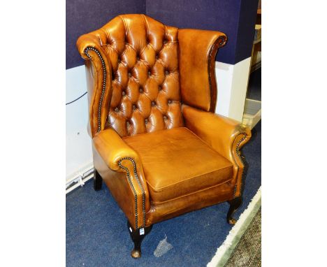 A tan leather library wing armchair, with studded and button back decoration, raised on cabriole supports, 109cm high x 84cm 