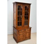 A reproduction oak cabinet with moulded cornice above the pair of glazed doors enclosing shelves,