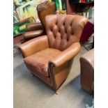 A modern brown leather tub chair with button back material.