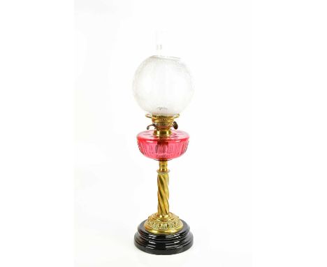 A Victorian brass oil lamp, with frosted glass bulbous shade and cranberry glass reservoir with faceted decoration, on a wryt