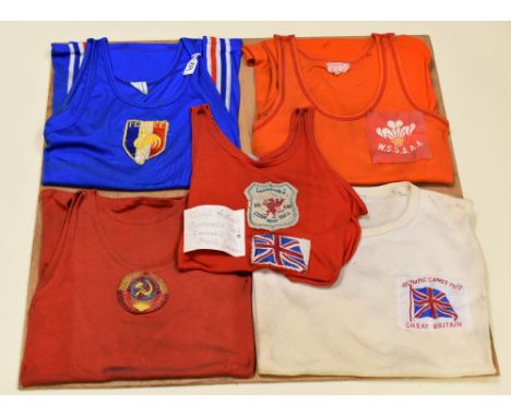 FOUR VINTAGE INTERNATIONAL GYMNASTIC VESTS & A GREAT BRITAIN 1972 T-SHIRT WITH STITCHED BADGE, pinned to a board for diaplay 