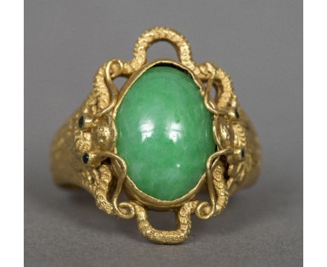 A Chinese 24 ct gold jade set ringThe stone cabochon cut, the shoulders worked as dragon masks with inset eyes.   CONDITION R