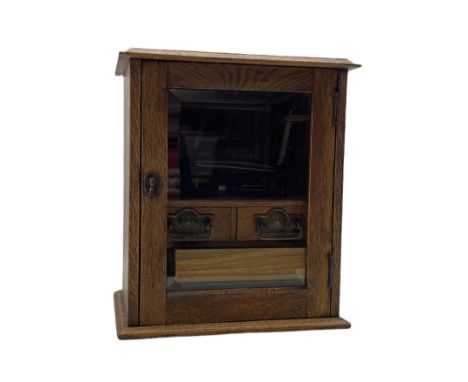 Early 20th century oak smokers cabinet with glazed hinged door enclosing two drawers and removable pipe rack in the form of a