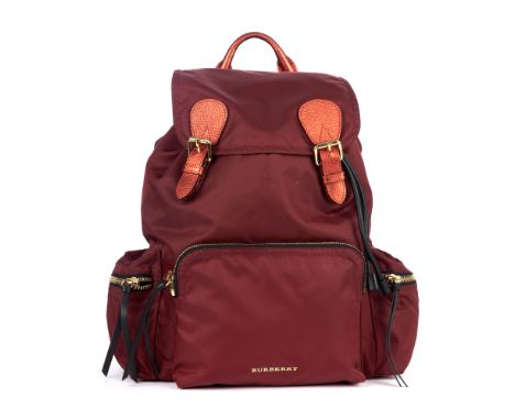 Burberry, a red nylon backpack, featuring metallic red leather trim and gold-tone hardware accents, with three exterior zip p