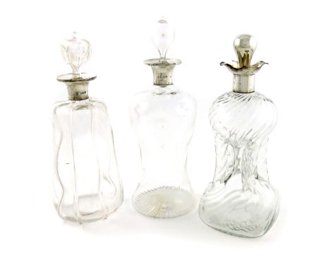 A collection of three silver-mounted glass decanters, comprising: an Edwardian one of shaped tapering form, ribbed decoration