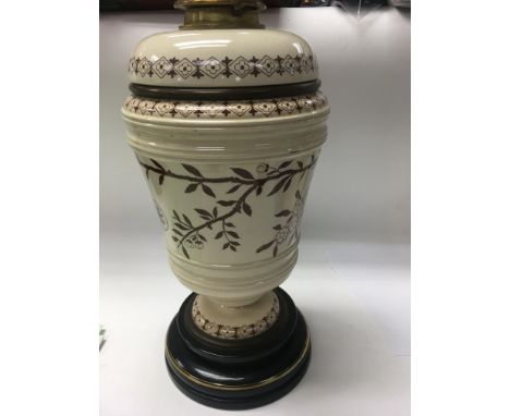 A Victorian oil lamp decorated with flowers and foliage on a brown glaze .