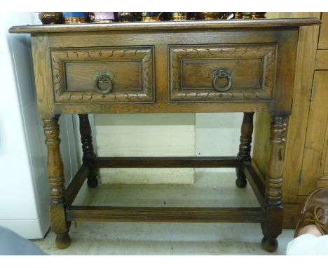 A modern Old English style oak side table, two in-line deep drawers with iron ring handles, raised on splayed, turned legs, u