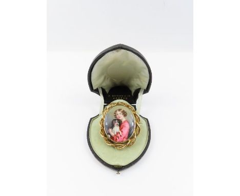 A Victorian ceramic panel brooch, depicting a child holding a spaniel, in a gold frame, 6.2 cm long, the mount testing as 18-