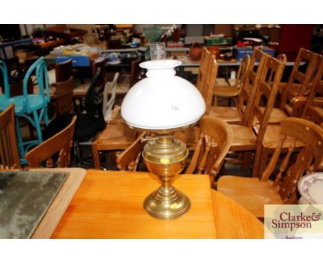 A brass oil lamp with an opaque glass shade and chimney