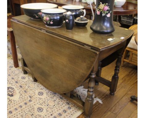 An early 20th century oak stained twin drop leaf dining table with gate leg action, oval top, raised on circular turned legs