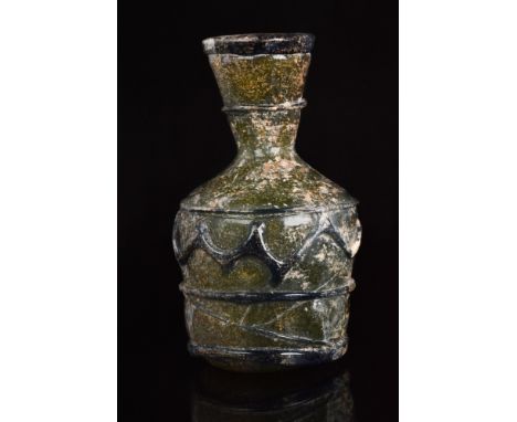 Ca. 300 AD. A yellowish glass flask featuring a squat body with a concave base, marked with a pontil scar, a funnel-shaped ne