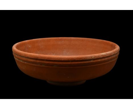 Ca. 300-400 AD. A small terra sigillata bowl of a wide body on a pedestal foot. The exterior is decorated with nicely incised