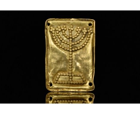 Ca. 100 AD. An amuletic plaque comprising of a rectangular sheet-gold plaque bearing a repoussé menorah, pierced in each corn