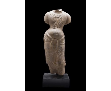 Ca. 549-577 AD (or later). A grey stone torso of a standing Buddha. The torso stands upright, and wears a light, billowing ro
