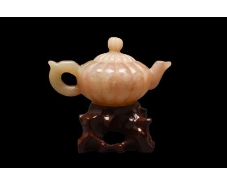 . A jade-carved teapot with a domed lid with a knob. It comes with a stand and a box. This is a particularly striking example