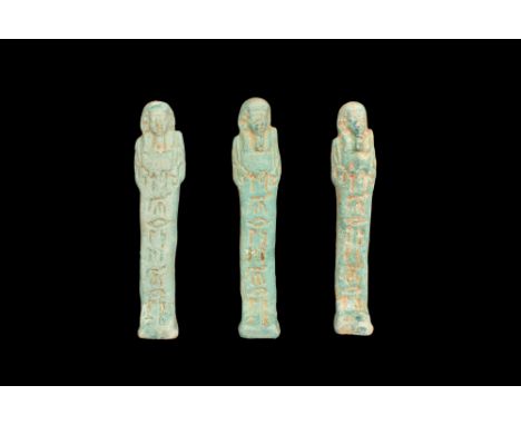 Late Period, 30th Dynasty, Ca. 332 BC. A group of three light blue faience ushabti figures, each wearing a tripartite wig, fa