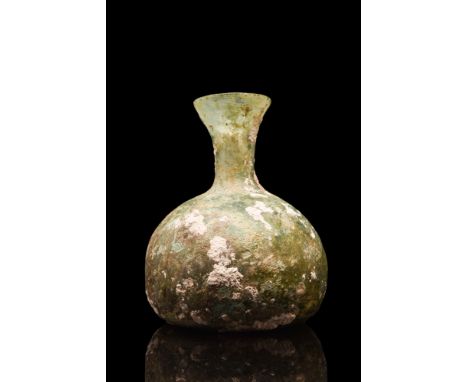 Ca. 100-300 AD. A free-blown glass flask of an apple-shaped lower body, concave base, and a tubular neck with everted rim. So