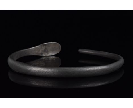 Ca. 1st Century AD. A silver flat-banded bracelet in penannular form, with one single terminal, the terminal in the form of a