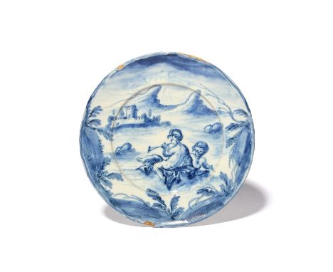 A Savona maiolica plate, late 17th/early 18th century, painted in blue with two putti reclining on rocks, one playing a long 