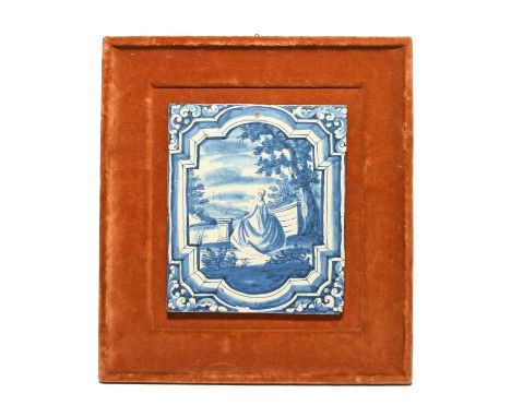 A Delft tile, 18th century, the rectangular form painted in blue with a lady on a garden terrace within a shaped border, with