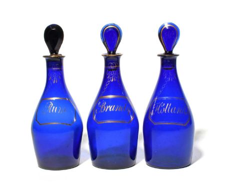 A set of three blue glass decanters and stoppers, c.1800, of mallet shape, each gilded with a chamfered bottle ticket various