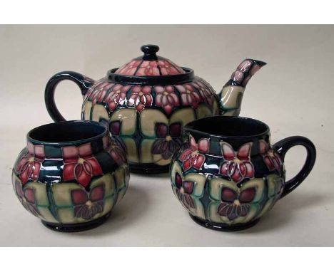 A Walter Moorcroft pottery three piece tea service, tubeline decorated in the Violet design by Sally Tuffin, comprises lidded