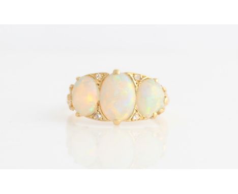 An opal and diamond ring, set with three graduated oval opal cabochons separated by four rose cut diamonds, with a scroll des