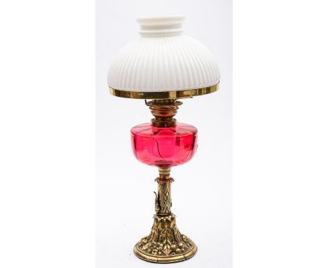 A late Victorian brass oil lamp with reeded opaque white glass shade and cranberry glass circular oil font, on foliate column