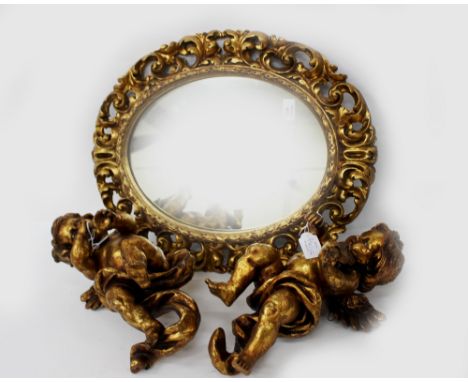A DECORATIVE OVAL WALL MIRROR with pierced scroll decorated frame, 43cm wide x 55cm high together with two gilt cherubs playi
