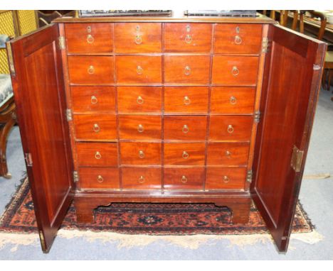 AN EDWARDIAN MAHOGANY CABINET OF DRAWERS with twin panelled doors opening to reveal twenty four short drawers each with brass